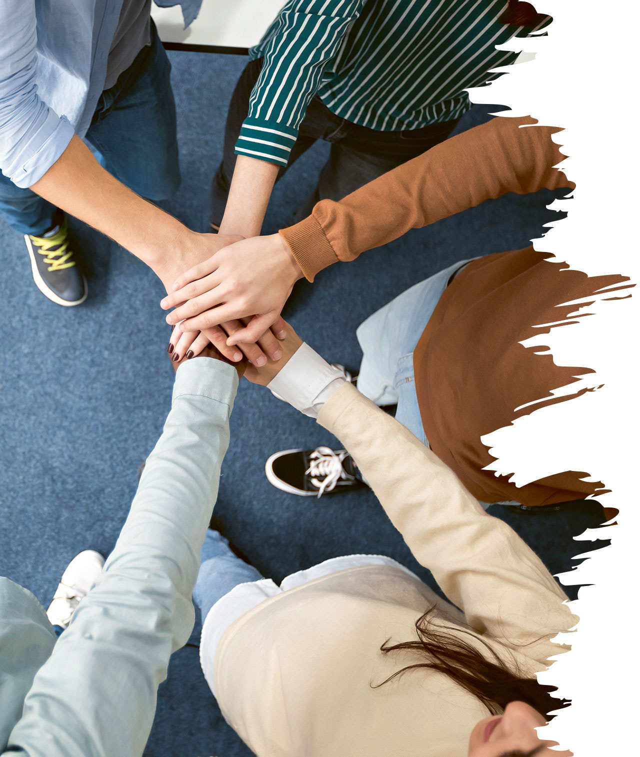 Fünf Personen stehen im Kreis und legen ihre Hände übereinander in die Mitte. Die Szene ist aus der Vogelperspektive aufgenommen.