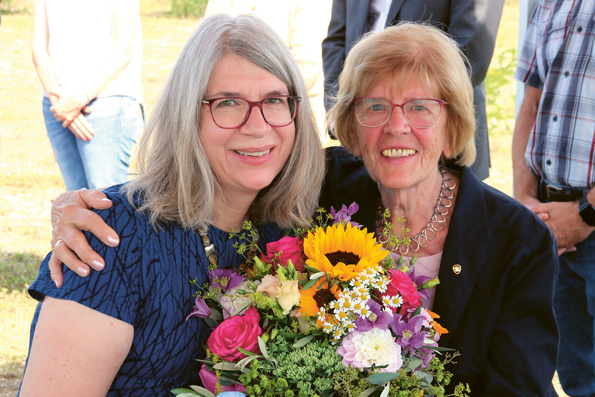 Prof. Dr. Bettina Wagner und ihre Mutter Irene Wagner lachen in die Kamera und halten einen Blumenstrauß mit vielen bunten Blumen in den Händen.
